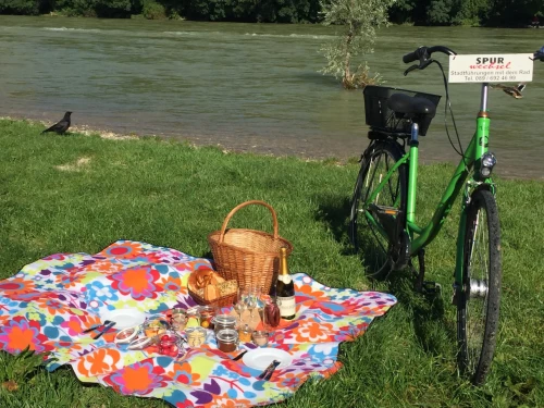 Spurwechsel Fahrradverleih, bike rental, green bike stands next to a colorful picnic blanket on which is a woven basket and all kinds of food