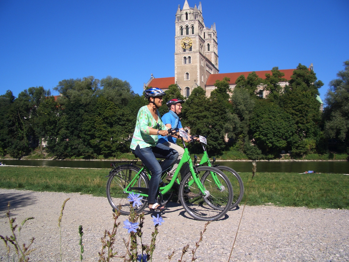 Spurwechsel Fahrradverleih, bike rental, Bicyclists ride along the Isar river, in the background you can see a big church