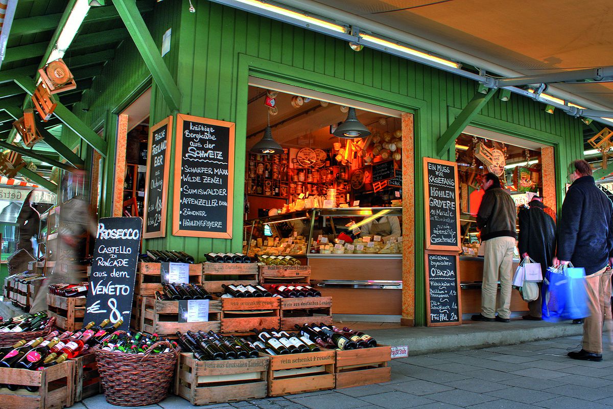 Laden am Viktualienmarkt mit Lbensmitteln, Wein, Käse und Menschen die in einer Schlange stehen