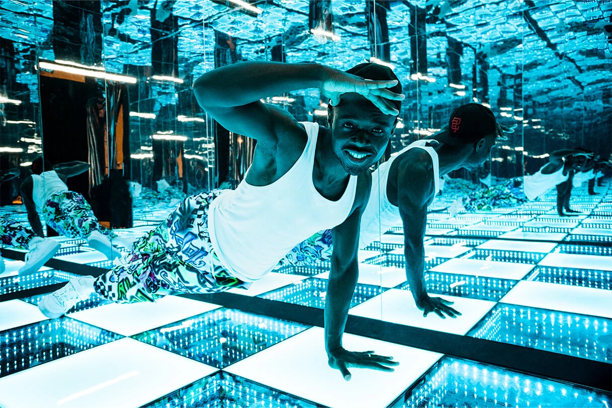 Studio of Wonders München, schwarzer Mann plankt in einem verspiegelten Raum und lacht in die Kamera, blaues Licht
