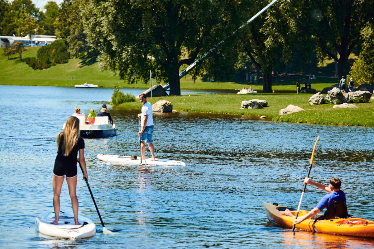 Two people stand on a stand up paddle on the Olympic lake, boats float next to them