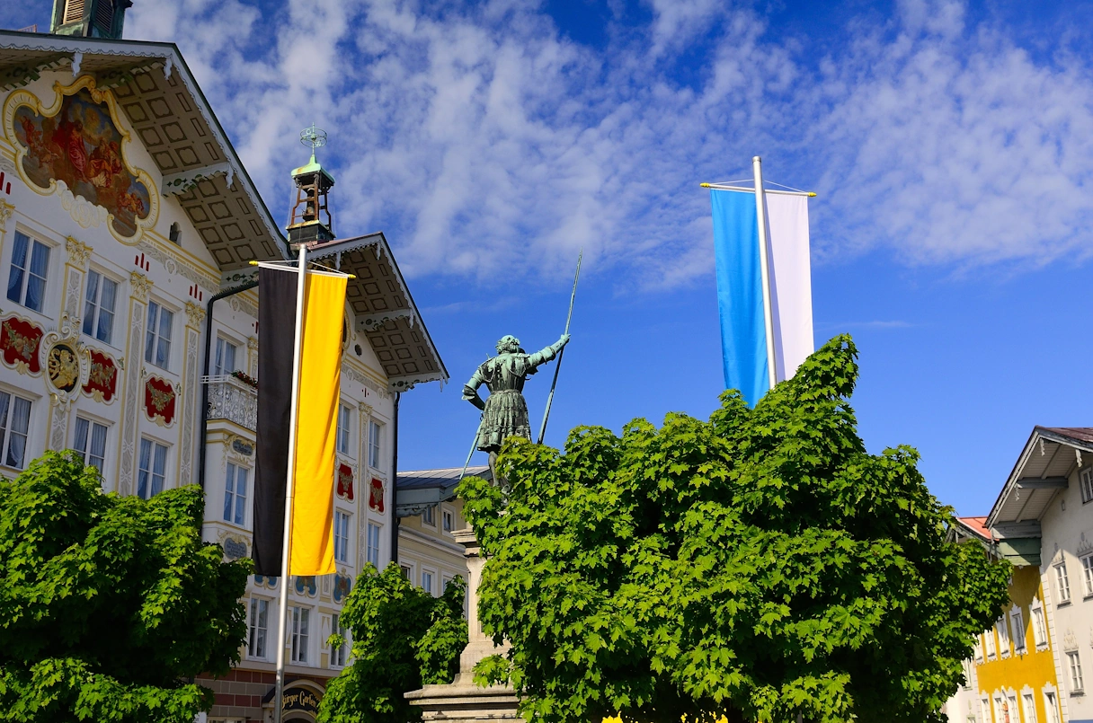 Tölzer Stadtmuseum von außen.Blick auf zwei Flaggen, eine Statue und Bäume