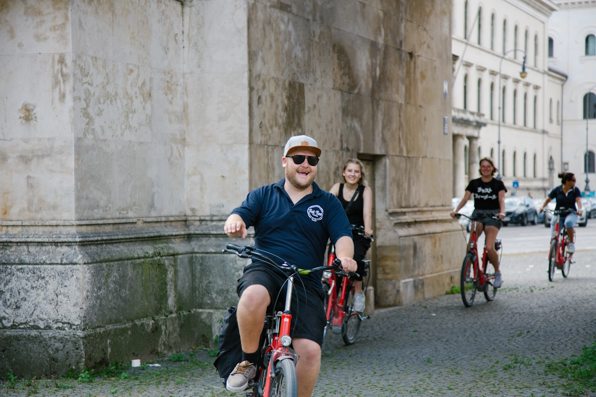 Fahrradtour zu viert in München. Voran fährt ein junger Mann mit Sonnenbrille und lacht. Dahinter fahren drei junge Frauen