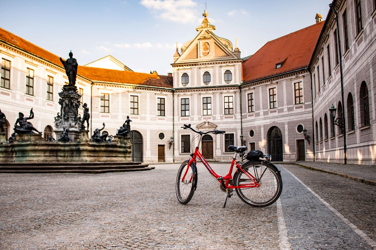 Ein rotes Fahrrad steht im Innenhof der Residenz München. In der Mitte ist ein Brunnen zu sehen